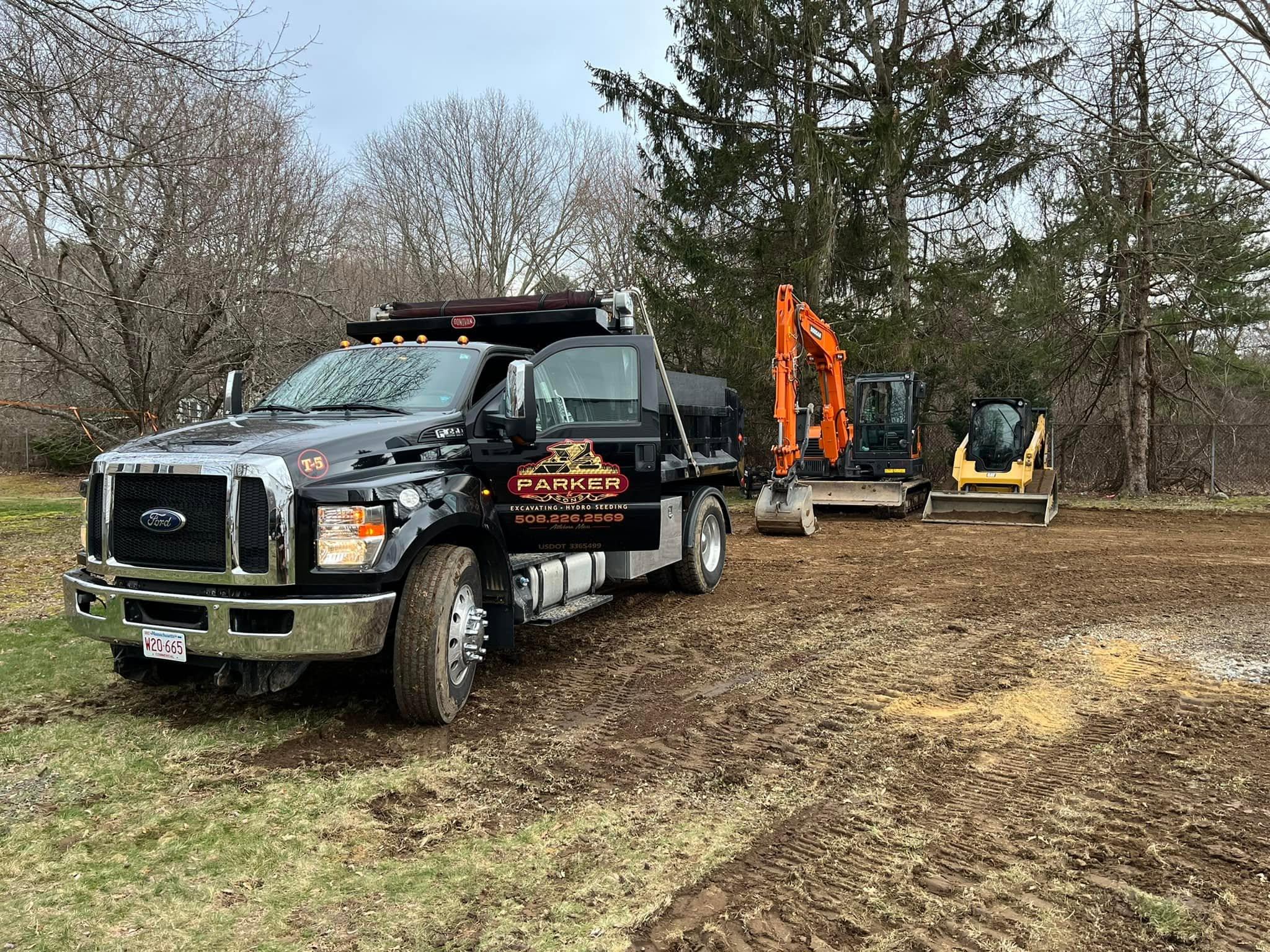 Branded Parker dump truck with excavators and a skid steer on a Massachusetts job site