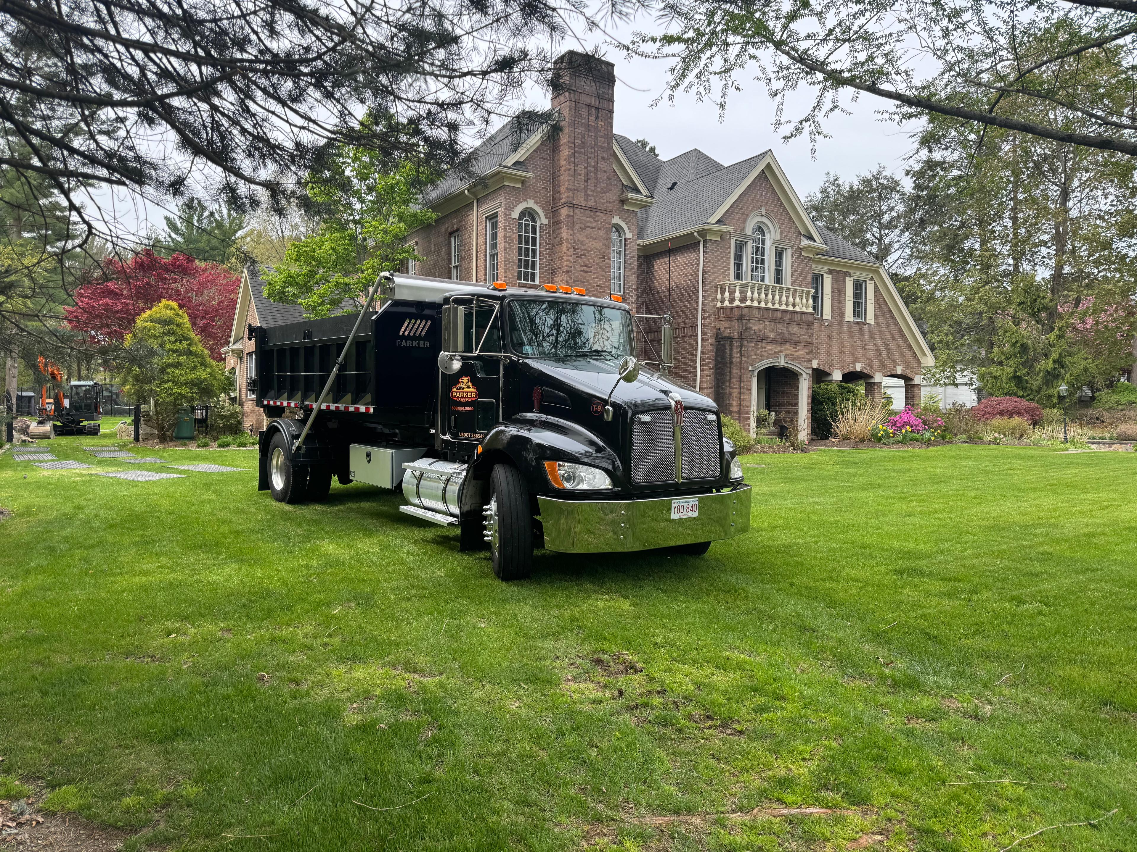 Parker & Sons branded dump truck at a landscaped residential property in Massachusetts