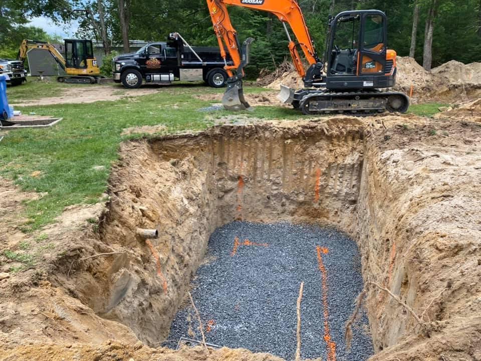 Prepared septic excavation with trucks and excavators staged around the work area
