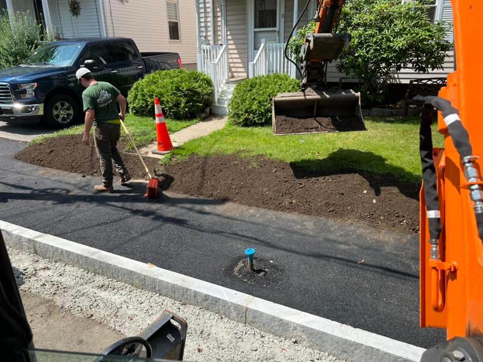 Crew member spreading topsoil beside a newly paved curb