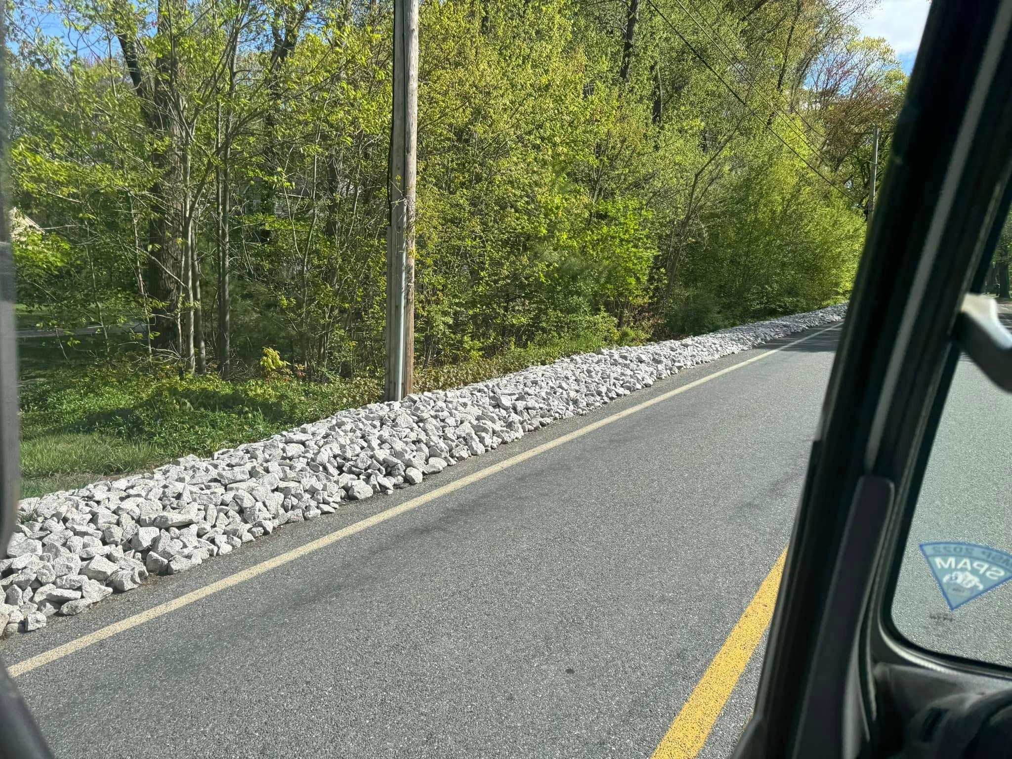 Completed roadside riprap drainage installation beside a wooded road