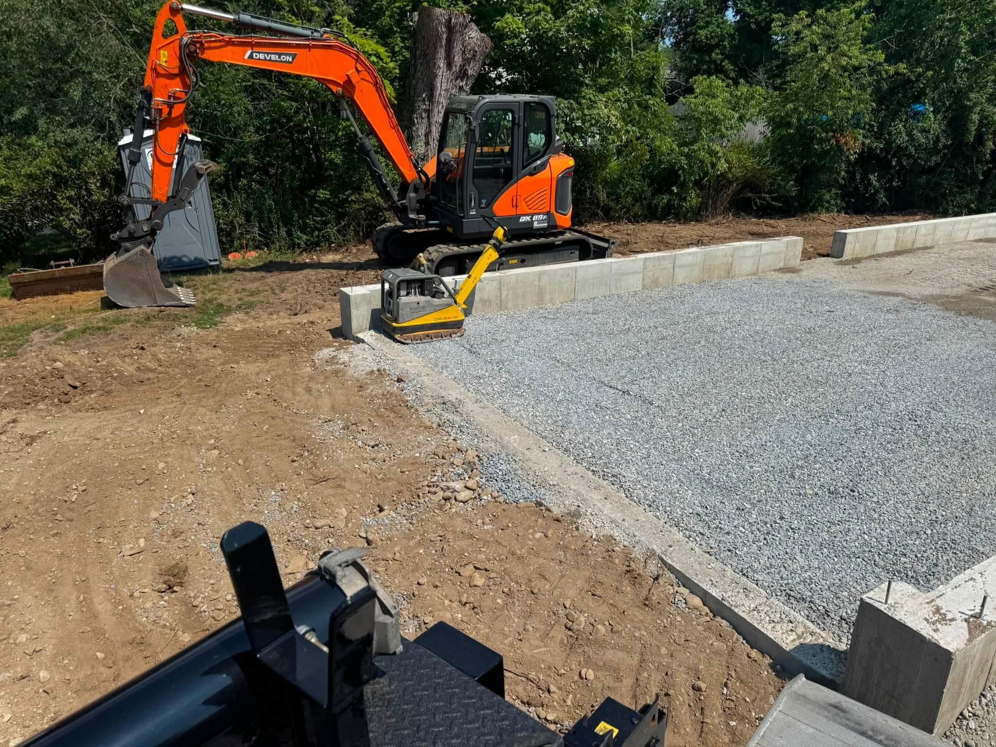 Excavator and compactor beside a prepared foundation gravel base