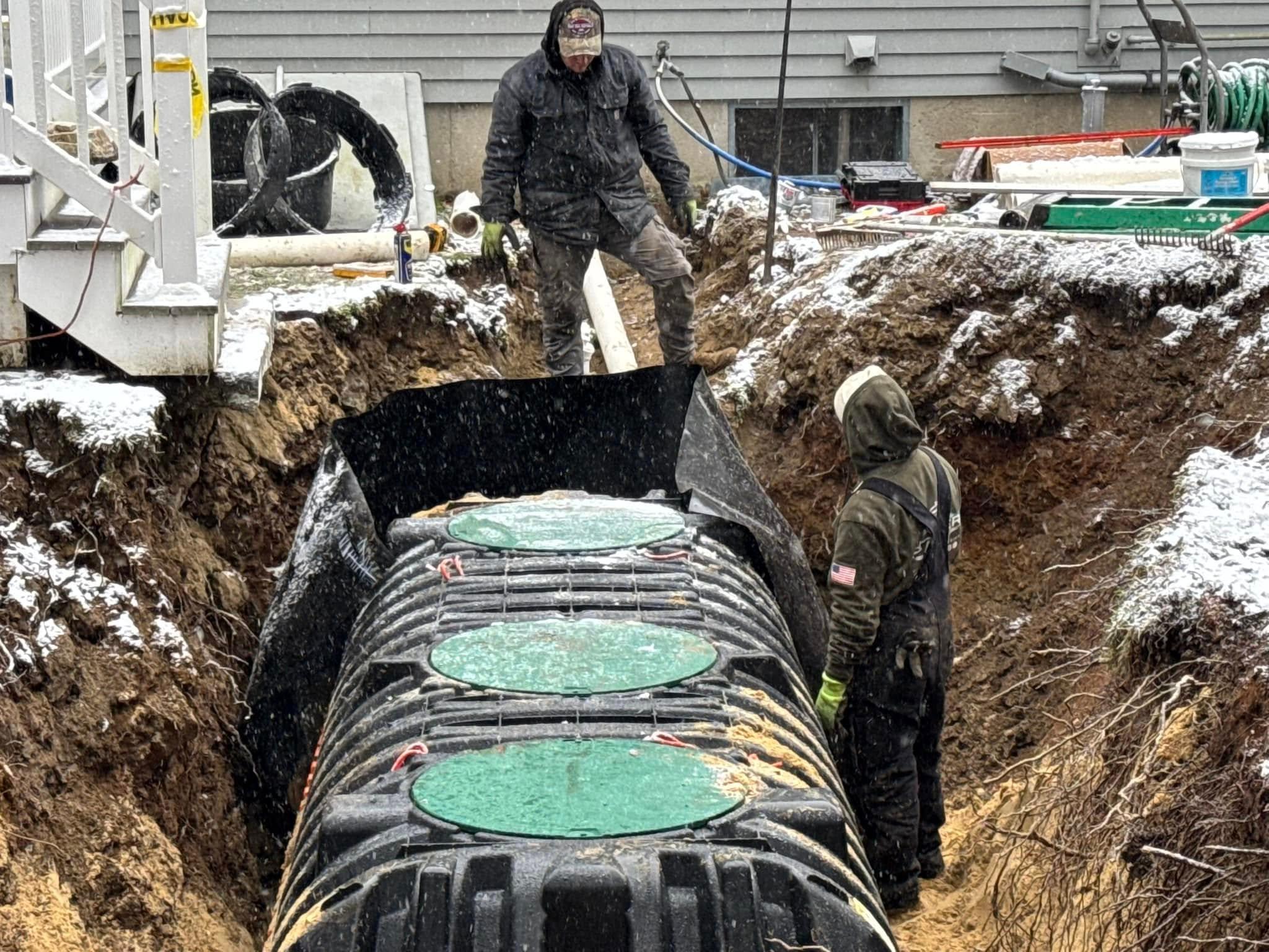 Crew members guiding a tank inside a snowy residential excavation